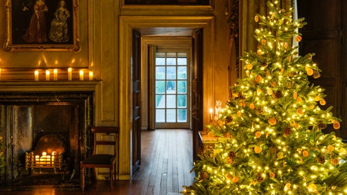 Christmas decorations and fireplace in the Volury at Ham House and Garden, Surrey with a view to the garden beyond and a Christmas tree in the foreground